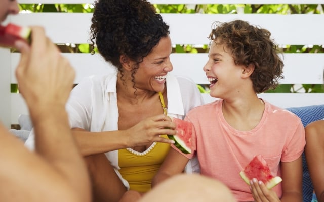mom and son laughing and eating watermelon in a poolside cabana on vacation in florida