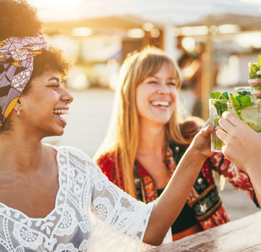 Women toasting with drinks and cocktails and having the sun and the beach on the background