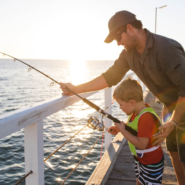 happy American father teaching little young son to be a fisherma