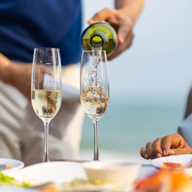 Waiter serving champagne to customers at beach restaurant.
