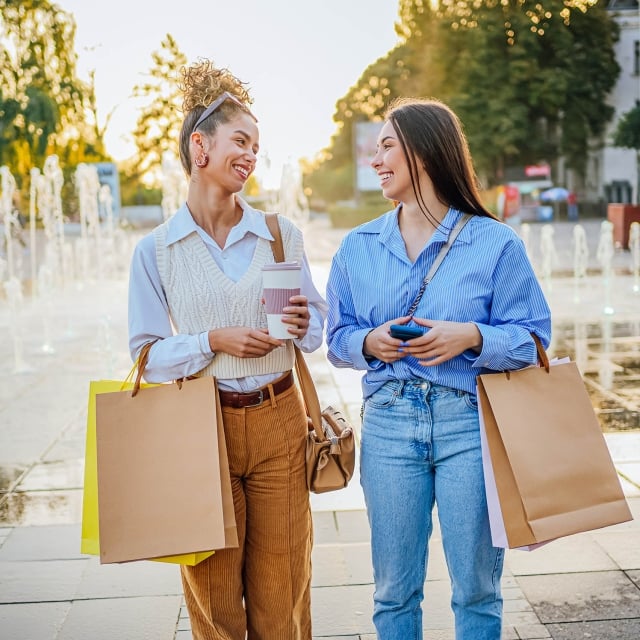 Cheerful young female friends walking together in the city after a successful shopping spree