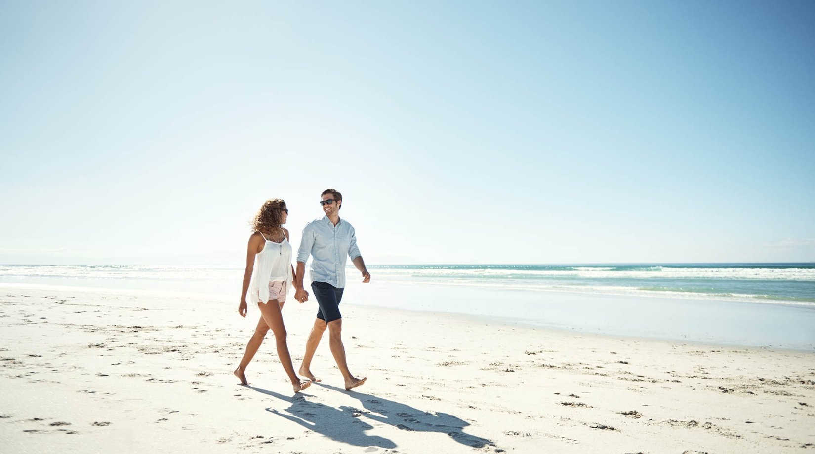 Shot of an affectionate young couple walking hand in hand on the beach